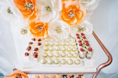 a table topped with lots of cupcakes covered in frosting and orange flowers