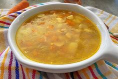 a white bowl filled with soup sitting on top of a table next to carrots