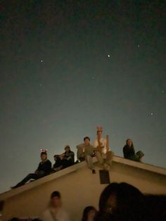 several people sitting on the roof of a building at night with stars in the sky