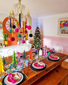 the table is set for christmas dinner with colorful decorations on it and plates in front