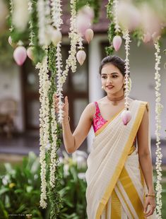 a woman in a yellow and white sari is standing under flowers with her hand up