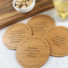 four wooden coasters with words on them sitting next to a bowl of nuts and a drink