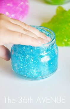 a hand reaching into a small jar filled with blue and green glitter