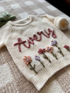 a knitted sweater with flowers and the words merry written on it sitting on a bed