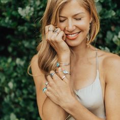 a woman smiles as she holds her hand to her face and wears rings on her fingers