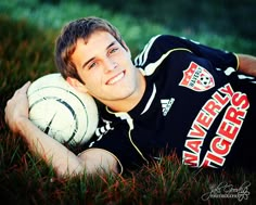 a young man laying in the grass with a soccer ball and smiling at the camera