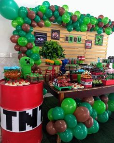 a table topped with lots of green and brown balloons next to a giant red barrel