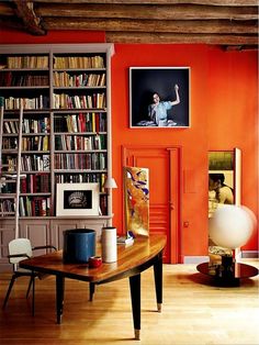 an orange room with bookshelves and a table in the middle, next to a book shelf full of books