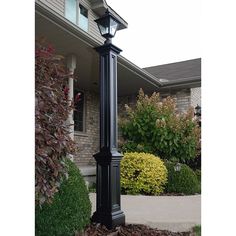 a black lamp post in front of a house with bushes and shrubs around the corner