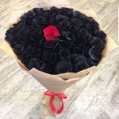 a bouquet of black roses wrapped in brown paper with a red ribbon on the end