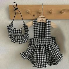 a black and white checkered dress hanging on a coat rack with two wooden pegs