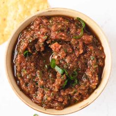 a bowl filled with meat and sauce next to some tortilla chips on the side