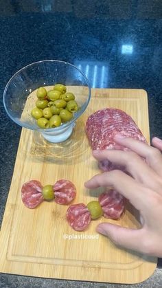 someone is cutting up some meat and olives on a wooden board next to a bowl of green olives