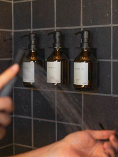 a person is spraying their hands with soap in front of three bottles on the wall