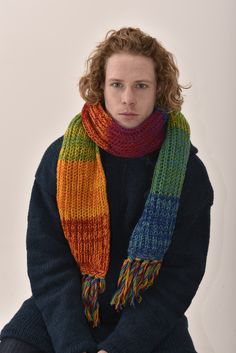 a man with curly hair wearing a multicolored knitted scarf and matching sweater