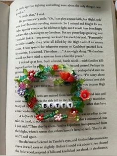 an open book with beads and flowers on it's pages that spell out the word betty