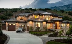 a car is parked in front of a large house at dusk with mountains in the background