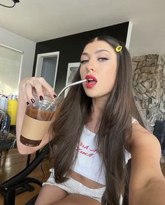 a woman sitting on the floor drinking from a cup with a straw in her mouth