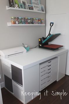 a white desk with drawers and a printer on it in a room that has shelving above the desk