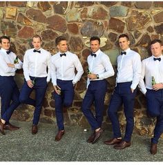 a group of men standing next to each other in front of a stone wall wearing white shirts and blue pants