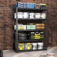 an industrial shelving unit with paint cans and buckets on the floor in front of a brick wall