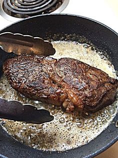 steak being cooked in a frying pan on top of the stove with tongs