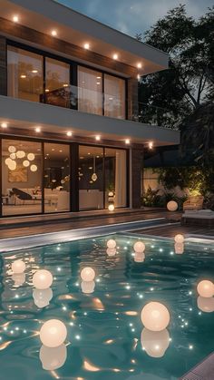 an outdoor pool with floating lights in the water next to a large house at night