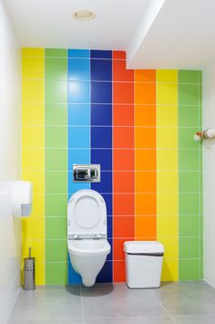 a bathroom with multicolored walls and a toilet in the middle, next to a trash can