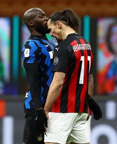 two men standing next to each other in front of a soccer field with the referee looking on