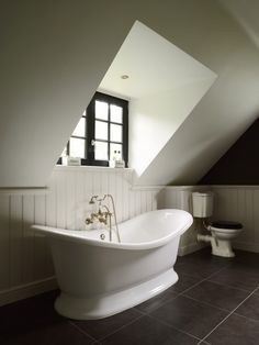 a white bath tub sitting under a window next to a toilet in a bathroom below a slanted ceiling