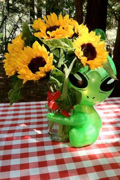 a green alien vase with sunflowers in it on a checkered table cloth