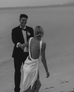 a man in a tuxedo and a woman in a dress walking on the beach