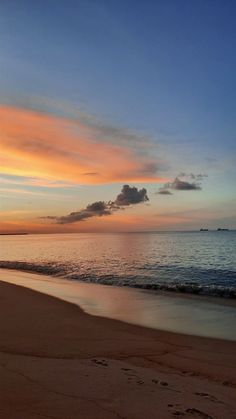 the sun is setting over the ocean with footprints in the sand