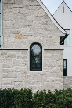 a stone building with a black window and green bushes in front of the windows is a white house