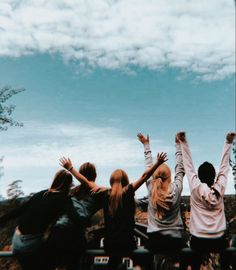 four people are sitting on a bench with their arms in the air