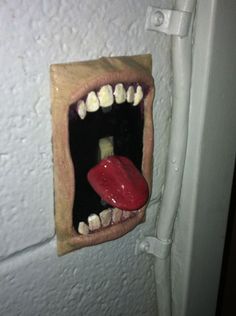 an open mouth with teeth and tongue sticking out from a hole in a white wall