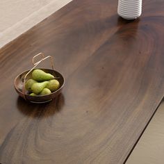 a bowl filled with green apples sitting on top of a wooden table next to a white vase