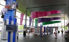 people are walking around in an open area with colorful banners hanging from the ceiling and bookshelves