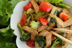 a white bowl filled with meat and veggies next to chopsticks in it