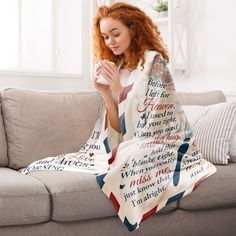 a woman sitting on a couch with a blanket over her face and holding a cup