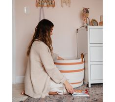 a woman sitting on the floor in front of a large white basket with an orange stripe