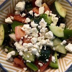 a salad with cucumbers, tomatoes and feta cheese in a striped bowl