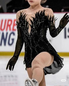 a female figure skating on the ice in a black dress with sequins and feathers