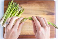 a person is cutting asparagus on a wooden board