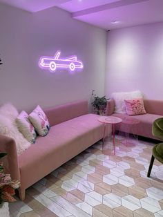 a living room with pink couches and pillows on the floor in front of a neon sign