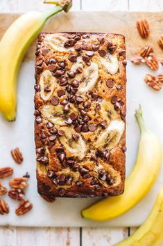 a loaf of banana bread with chocolate chips and pecans around it on a cutting board