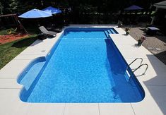 an empty swimming pool with chairs and umbrellas in the back yard, next to a fence