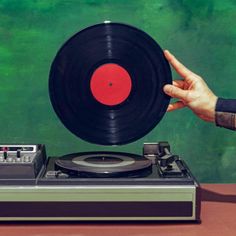 a person holding a record player in front of a green background with red and black discs