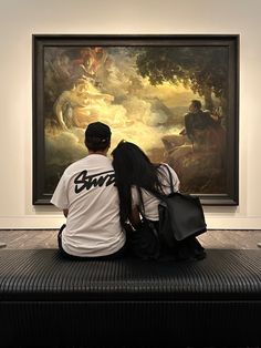 two people are sitting on a bench looking at a painting in an art museum,