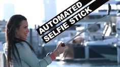 a woman is fishing on the water with boats in the background and an automated selfie stick over her head